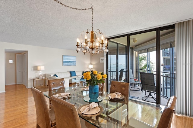 dining room with light hardwood / wood-style flooring, a wall of windows, a textured ceiling, and an inviting chandelier