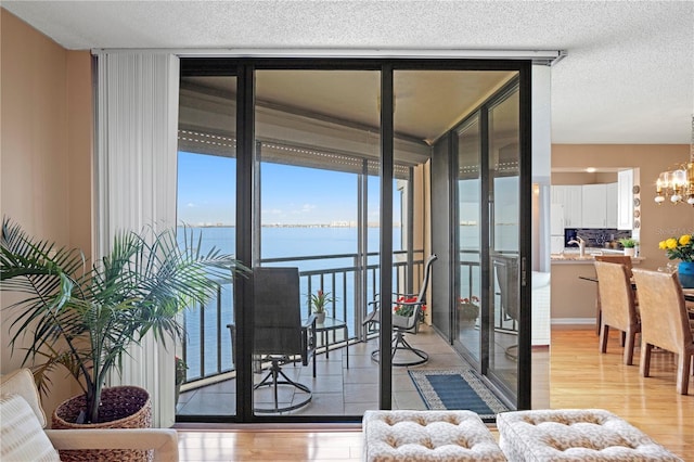 doorway to outside featuring a water view, a textured ceiling, light wood-type flooring, a notable chandelier, and a wall of windows