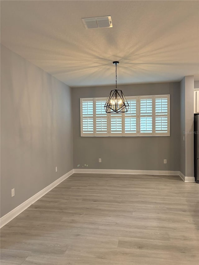 unfurnished dining area featuring an inviting chandelier and light wood-type flooring