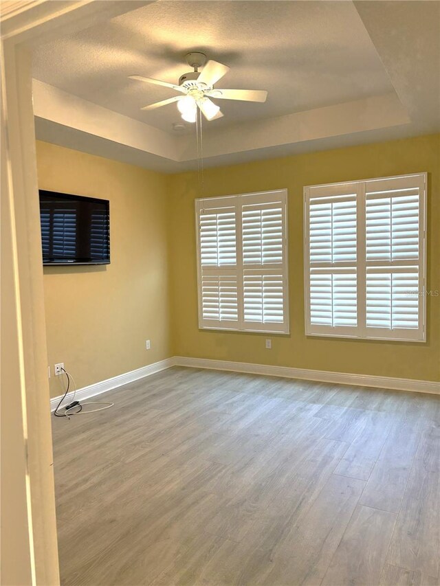 spare room with a raised ceiling, ceiling fan, and light wood-type flooring