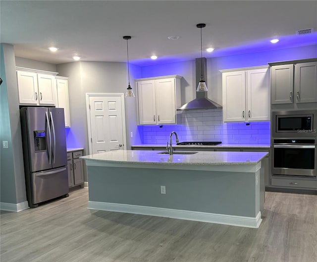 kitchen featuring stainless steel appliances, decorative light fixtures, a kitchen island with sink, and wall chimney range hood