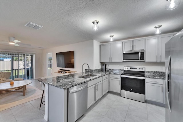 kitchen with light tile patterned flooring, sink, dark stone counters, kitchen peninsula, and stainless steel appliances