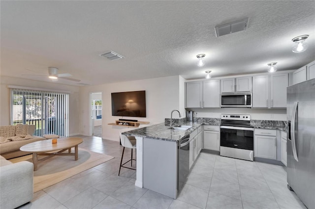 kitchen featuring sink, a breakfast bar area, dark stone countertops, stainless steel appliances, and kitchen peninsula