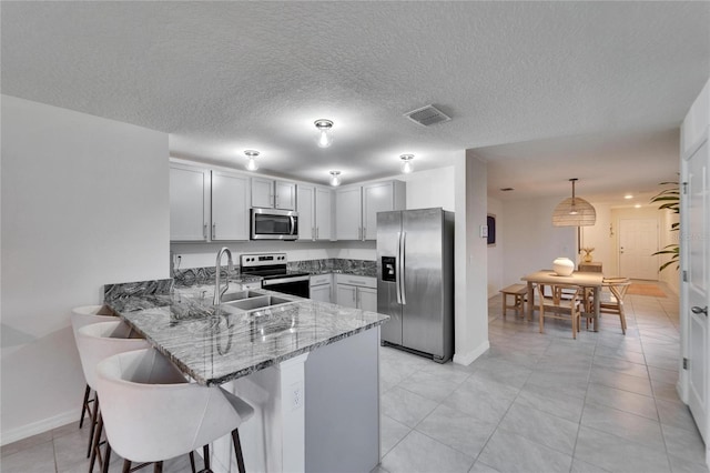 kitchen featuring sink, stainless steel appliances, decorative light fixtures, kitchen peninsula, and dark stone counters