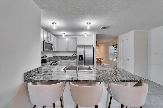 kitchen featuring sink, a breakfast bar, appliances with stainless steel finishes, dark stone countertops, and kitchen peninsula