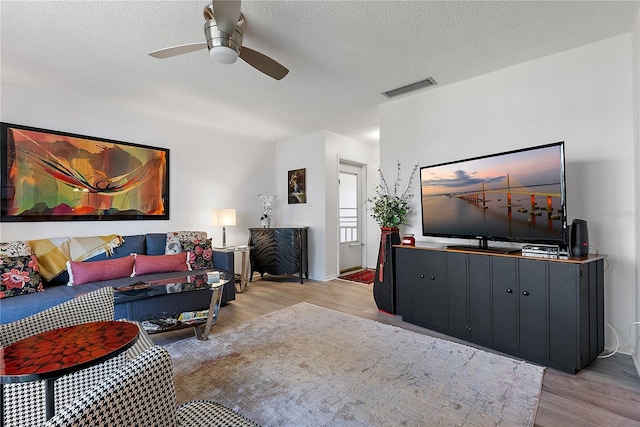 living room with ceiling fan, a textured ceiling, and light wood-type flooring