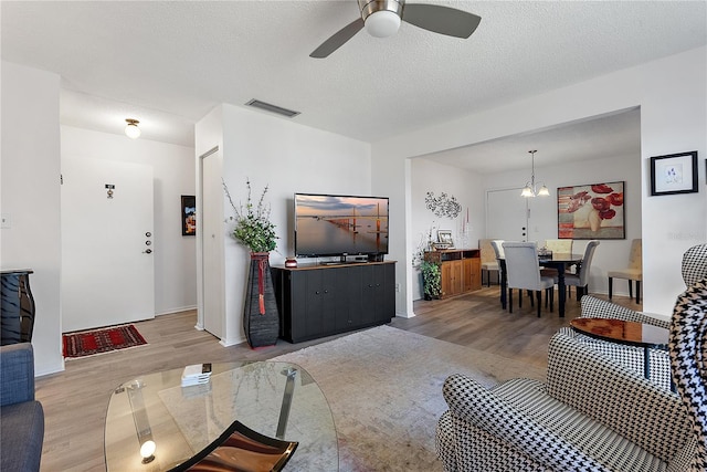 living room with wood-type flooring, ceiling fan with notable chandelier, and a textured ceiling