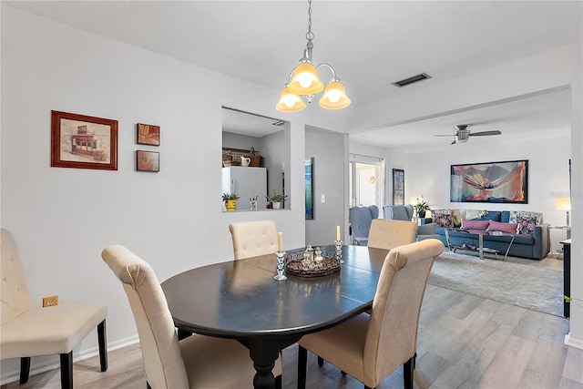 dining area with ceiling fan with notable chandelier and light hardwood / wood-style flooring