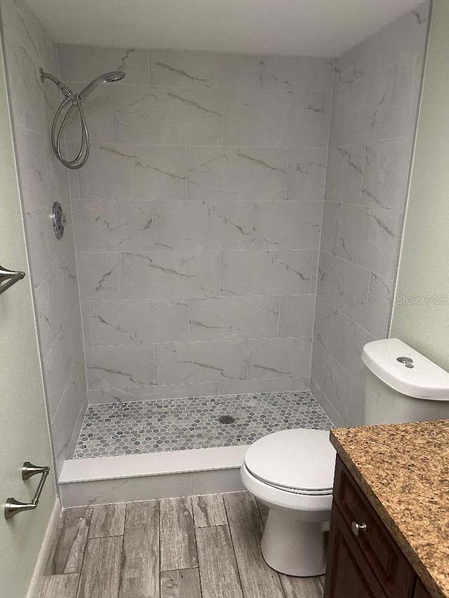 bathroom featuring vanity, a tile shower, and toilet