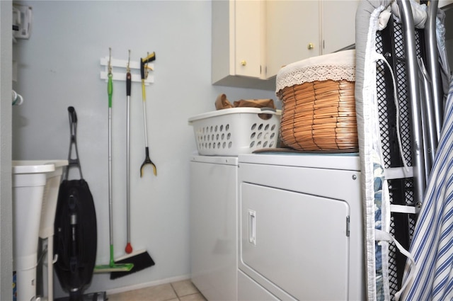 clothes washing area with light tile patterned floors, washing machine and dryer, and cabinets