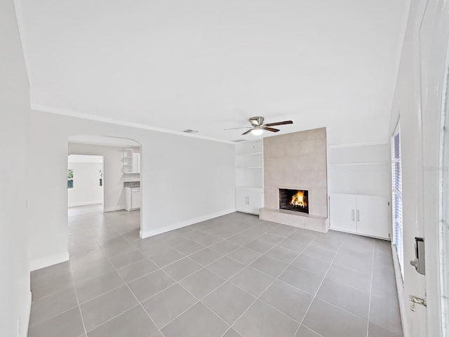 unfurnished living room with ceiling fan, a large fireplace, crown molding, and light tile patterned floors