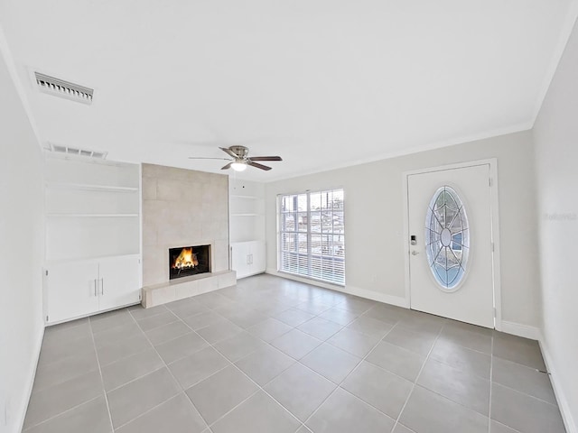 unfurnished living room with light tile patterned floors, built in features, ceiling fan, ornamental molding, and a tiled fireplace