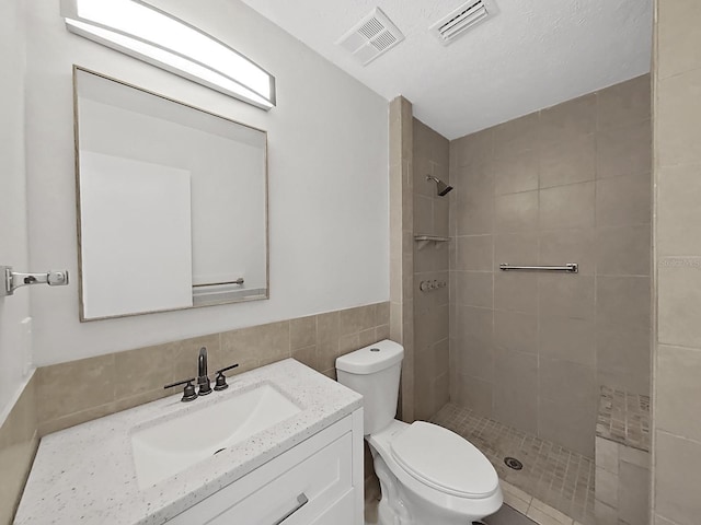 bathroom featuring vanity, tile walls, toilet, and tiled shower