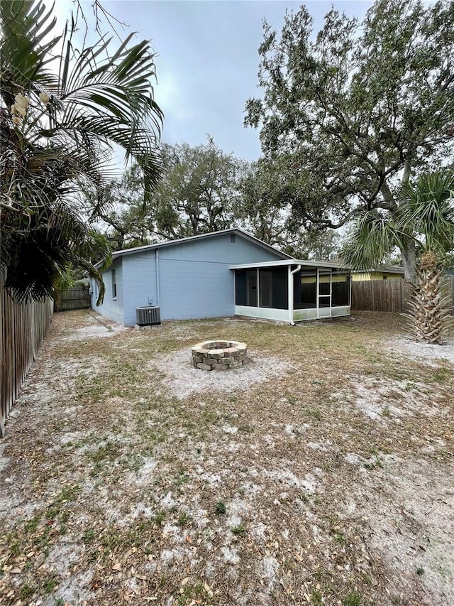 rear view of house with a sunroom, central AC unit, and a fire pit