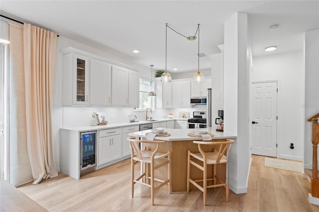 kitchen with a breakfast bar area, appliances with stainless steel finishes, white cabinetry, wine cooler, and light wood-type flooring