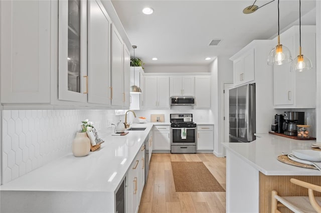 kitchen with appliances with stainless steel finishes, pendant lighting, sink, white cabinets, and decorative backsplash