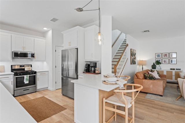 kitchen featuring appliances with stainless steel finishes, decorative light fixtures, light wood-type flooring, and white cabinets