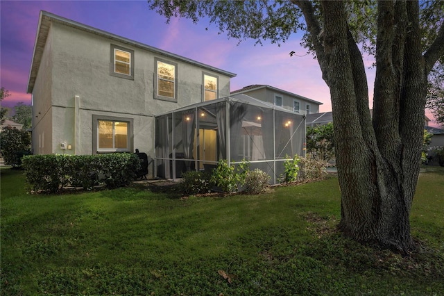 back house at dusk with a lawn and glass enclosure