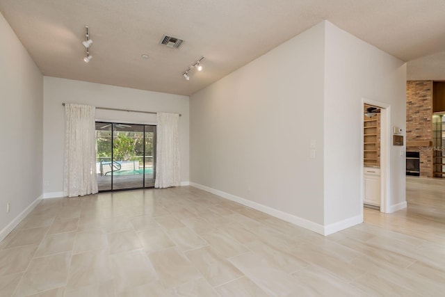 spare room with a large fireplace, track lighting, and a textured ceiling