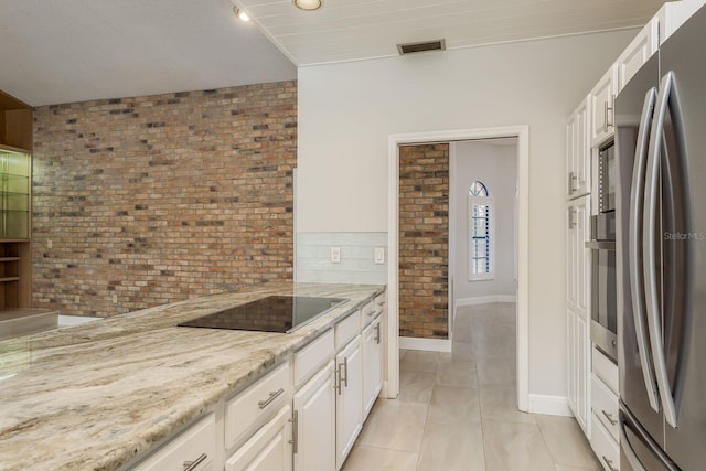 kitchen featuring brick wall, appliances with stainless steel finishes, white cabinets, light tile patterned floors, and light stone countertops