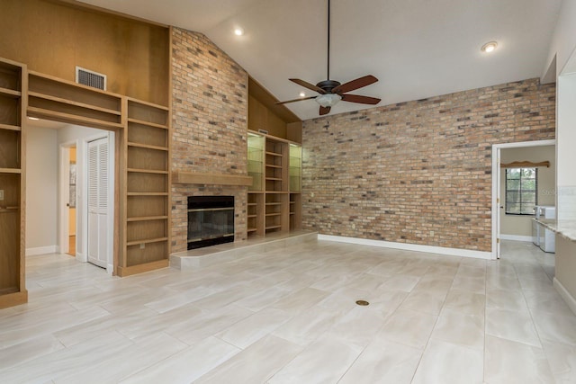 unfurnished living room with built in shelves, brick wall, a tiled fireplace, and high vaulted ceiling