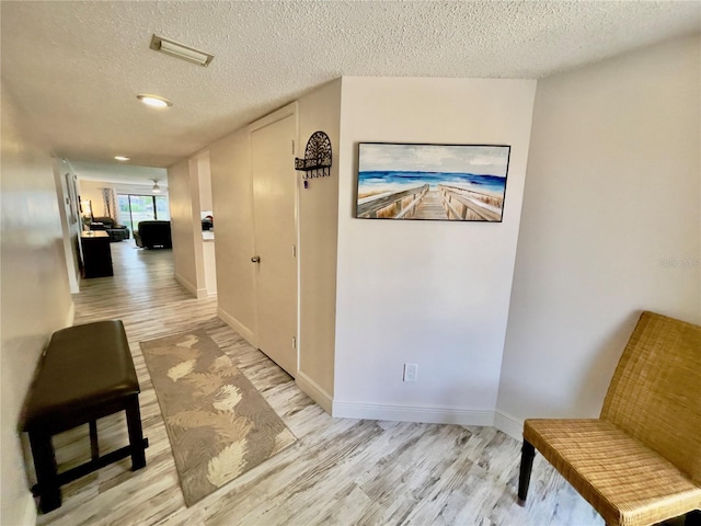 hall with a textured ceiling and light hardwood / wood-style flooring