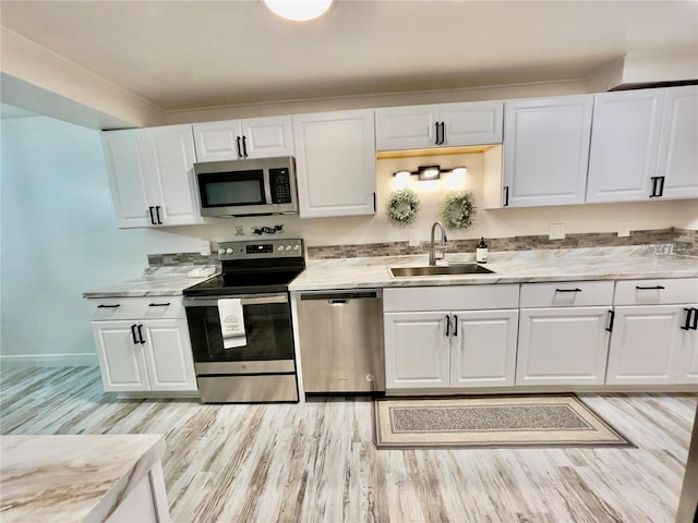 kitchen featuring sink, white cabinetry, light wood-type flooring, stainless steel appliances, and light stone countertops