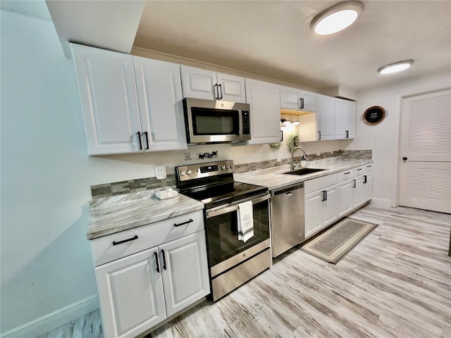 kitchen featuring sink, stainless steel appliances, light stone counters, light hardwood / wood-style floors, and white cabinets