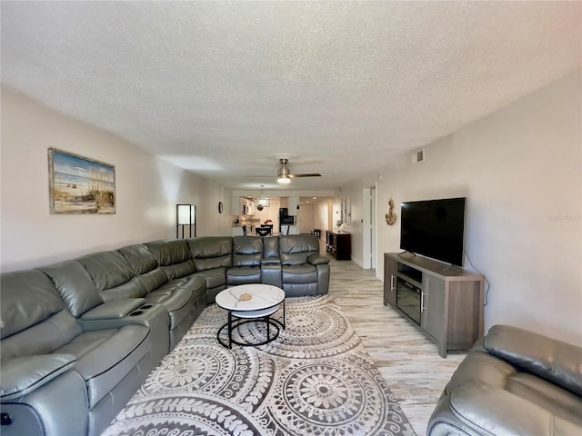 living room featuring ceiling fan, a textured ceiling, and light wood-type flooring