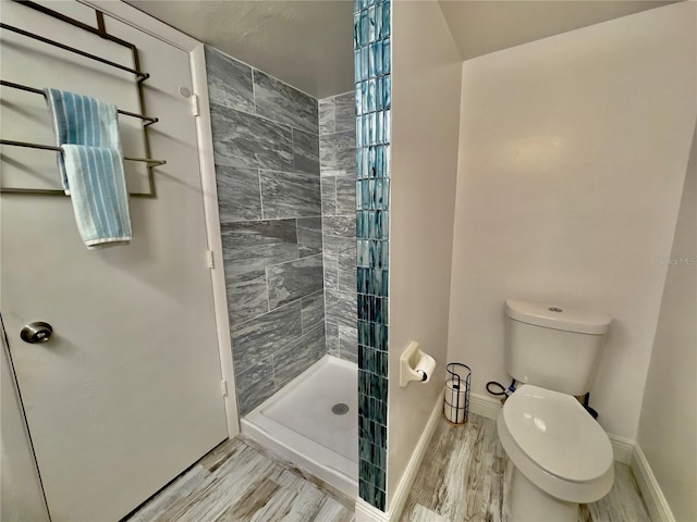 bathroom featuring a tile shower, wood-type flooring, and toilet