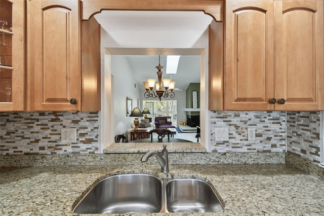 kitchen featuring light stone counters, a notable chandelier, backsplash, and a sink