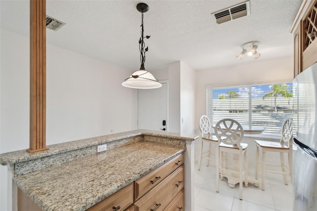 kitchen featuring visible vents, a textured ceiling, freestanding refrigerator, and light stone countertops