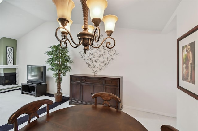 dining space featuring baseboards, lofted ceiling, an inviting chandelier, and a glass covered fireplace