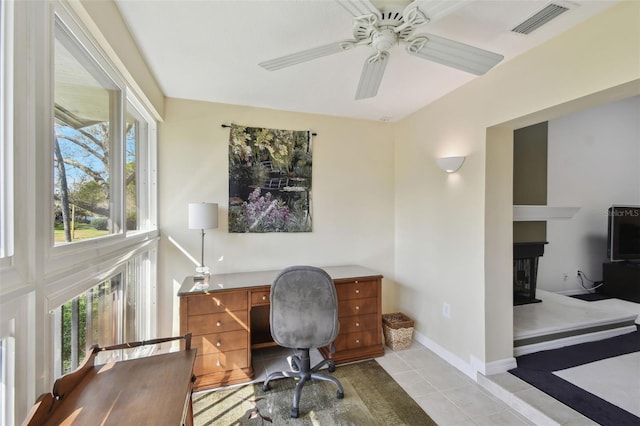 office area with a ceiling fan, visible vents, baseboards, light tile patterned flooring, and a glass covered fireplace