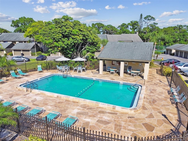 community pool with an outdoor structure, a patio area, and fence