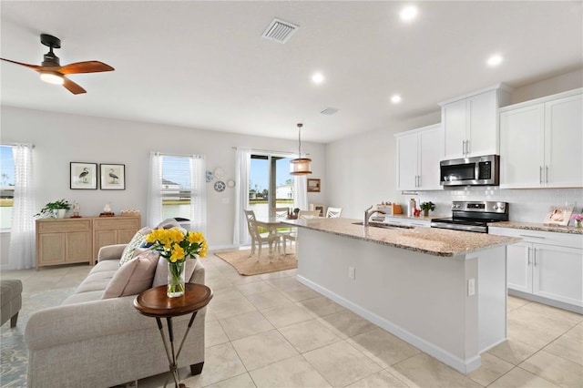 kitchen with pendant lighting, appliances with stainless steel finishes, white cabinetry, a kitchen island with sink, and light stone counters