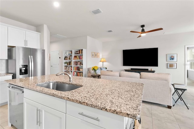 kitchen with sink, stainless steel appliances, light stone counters, white cabinets, and a center island with sink