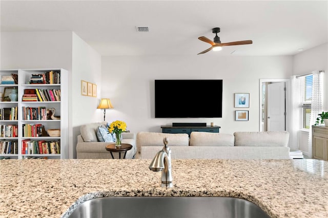 kitchen featuring ceiling fan, sink, and light stone counters