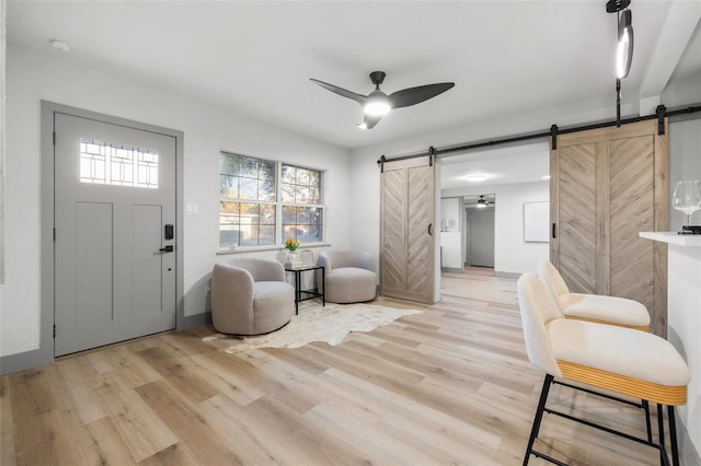 foyer entrance with ceiling fan, a barn door, and light wood-type flooring