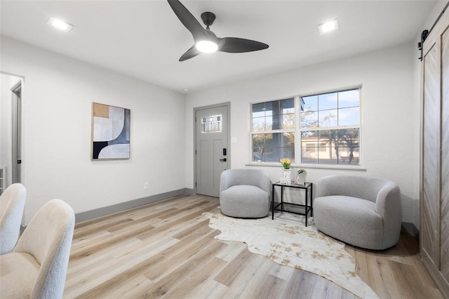 living area with ceiling fan, a barn door, and light hardwood / wood-style flooring