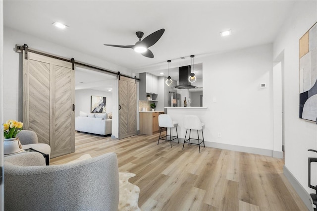 living room featuring a barn door, ceiling fan, and light hardwood / wood-style flooring