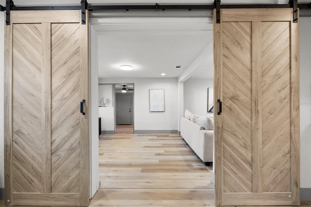 corridor with a barn door and light hardwood / wood-style floors