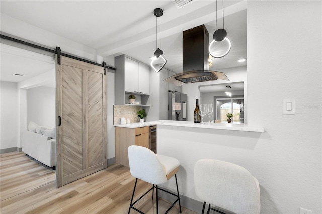 kitchen featuring island range hood, decorative light fixtures, white cabinets, stainless steel refrigerator with ice dispenser, and a barn door