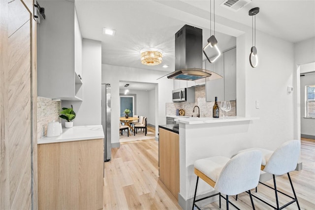 kitchen with pendant lighting, tasteful backsplash, island exhaust hood, stainless steel appliances, and light hardwood / wood-style flooring