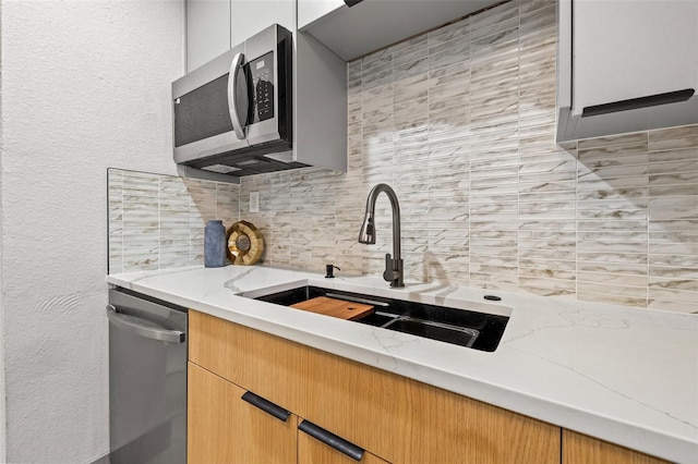 kitchen with sink, decorative backsplash, light stone countertops, and appliances with stainless steel finishes