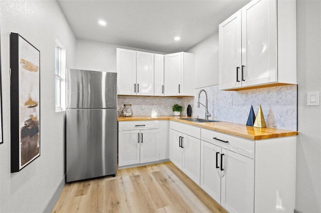 kitchen with sink, stainless steel refrigerator, wooden counters, white cabinetry, and light hardwood / wood-style floors