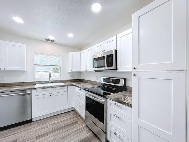 kitchen featuring appliances with stainless steel finishes, sink, white cabinets, light hardwood / wood-style floors, and a textured ceiling