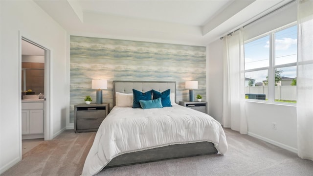 bedroom featuring light colored carpet, ensuite bathroom, and a raised ceiling