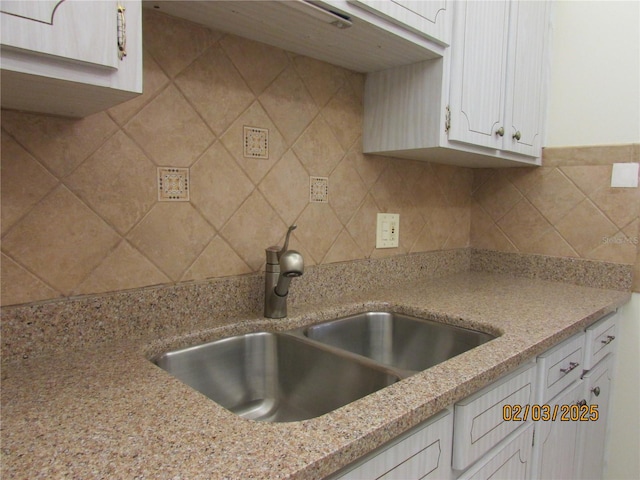 kitchen featuring light stone counters, sink, decorative backsplash, and white cabinets