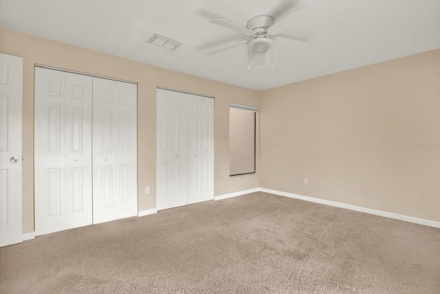 unfurnished bedroom featuring multiple closets, carpet floors, and ceiling fan